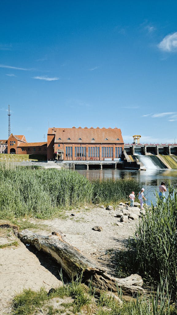 Hydroelectric power station with people enjoying nature nearby on a sunny day.