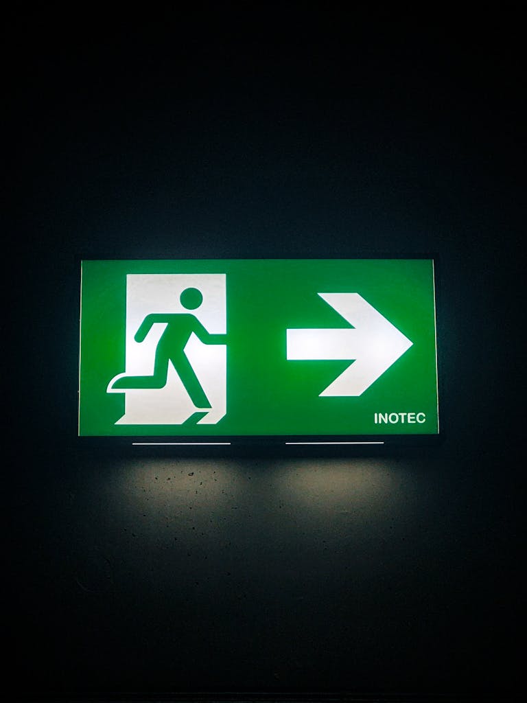 Illuminated green emergency exit sign with directional arrow in a dark indoor setting.