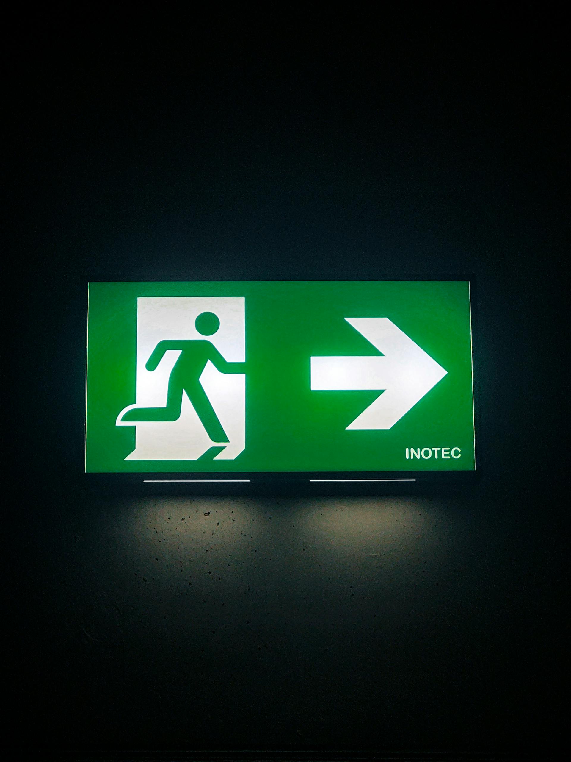 Illuminated green emergency exit sign with directional arrow in a dark indoor setting.
