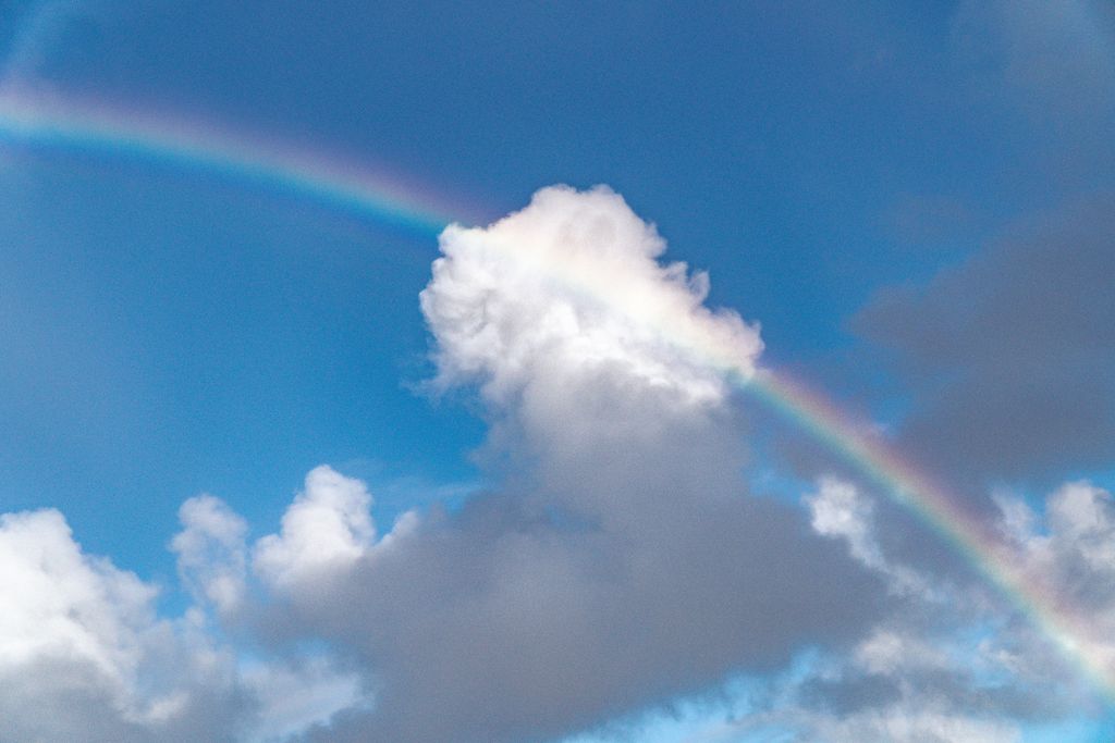 A vibrant rainbow arcs across a bright blue sky with fluffy clouds, perfect for nature-themed projects.